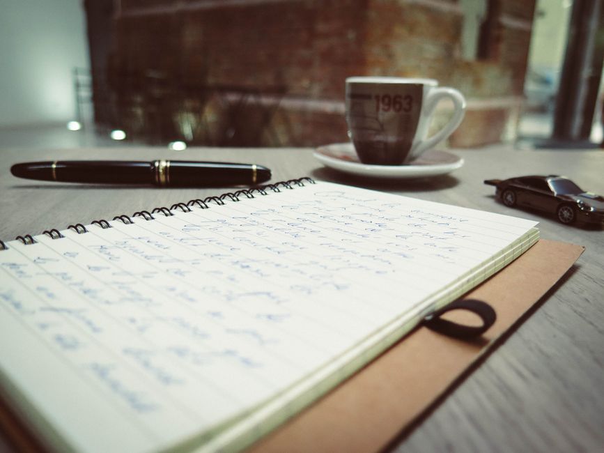 a person writing notes with a pen in a blank notebook on a wooden table