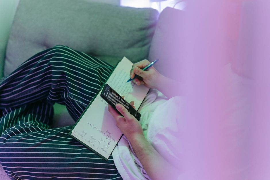 person writing notes while looking at a smartphone