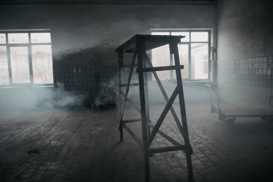 Eerie abandoned room filled with smoke, featuring a wooden ladder and large windows.