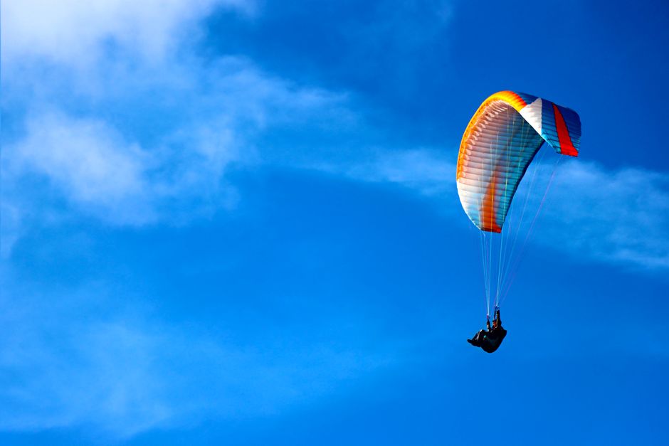 A solitary paraglider soars through a bright blue sky, capturing the thrill of flight and adventure.