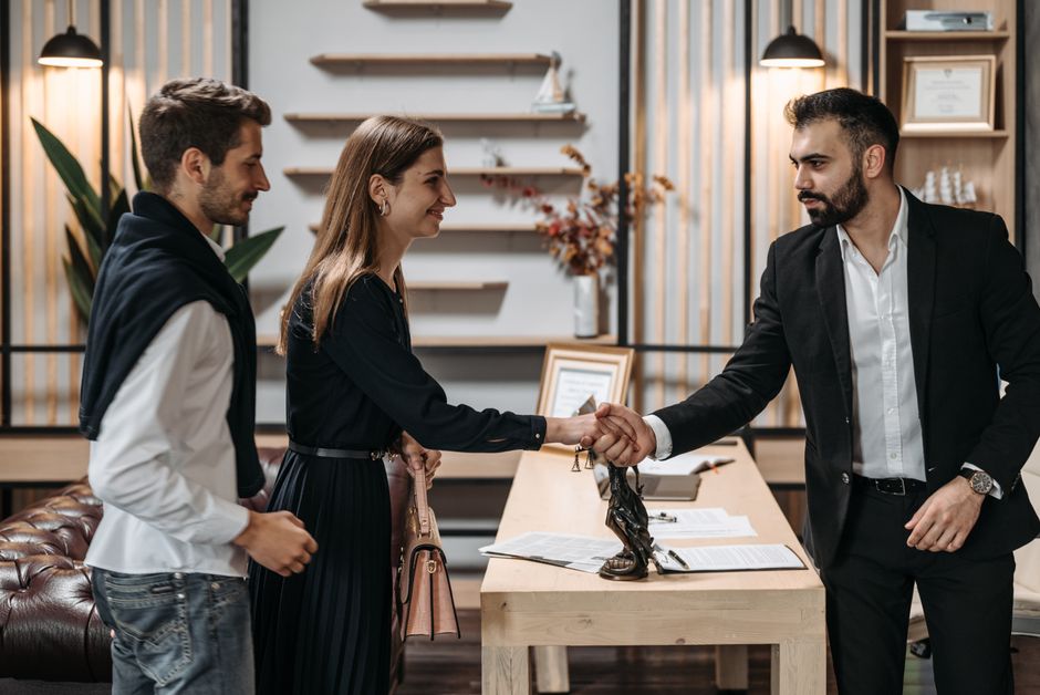 A professional meeting in a modern office with a couple shaking hands with a businessman.