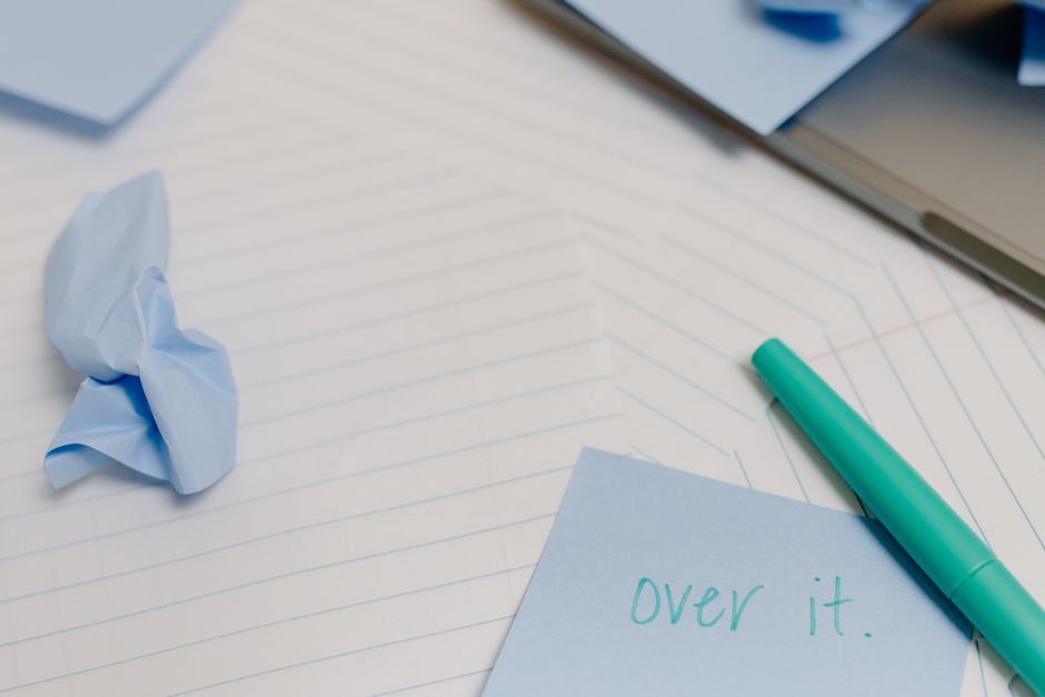 Overhead view of a desk with blue sticky notes, crumpled paper, and a green pen.