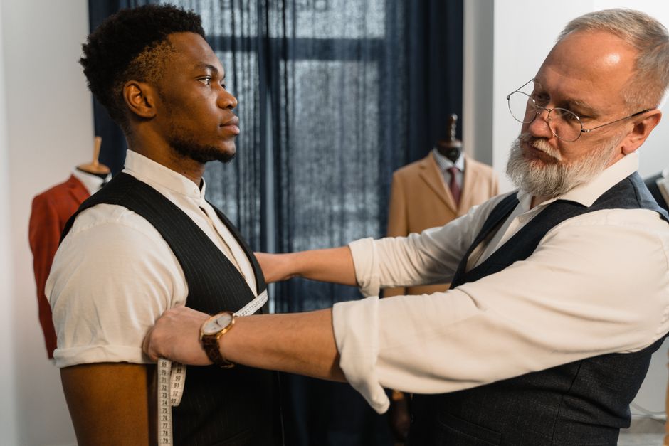 Professional tailor takes measurements for a bespoke suit fitting in a tailoring workshop.