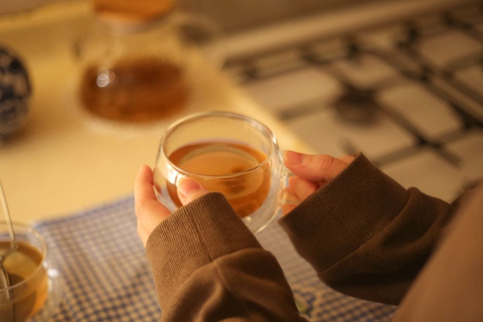 Close-up of a person holding a glass cup of tea in a cozy kitchen setting.