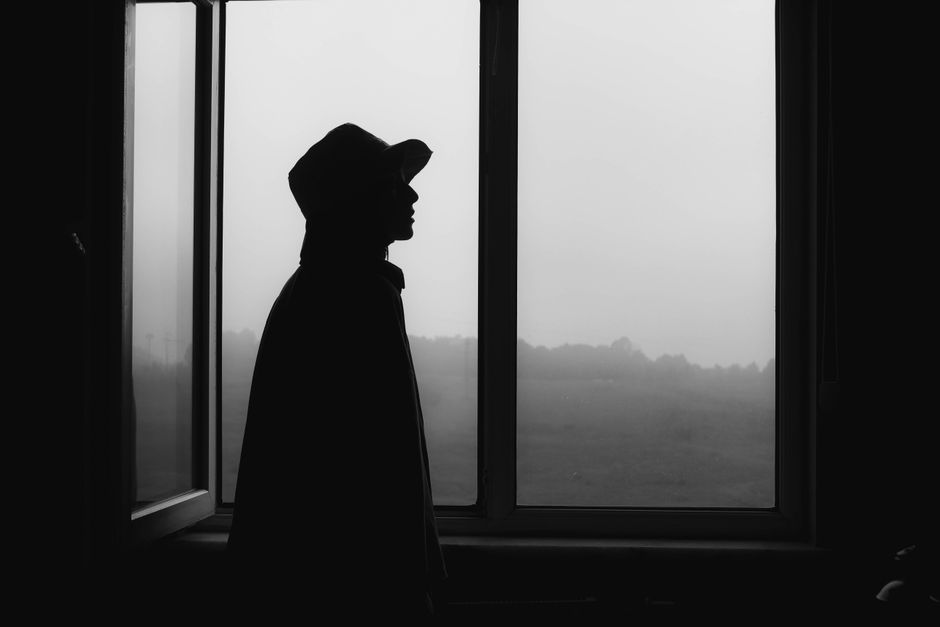 Moody black and white silhouette of a person standing by a window, creating a dramatic effect.
