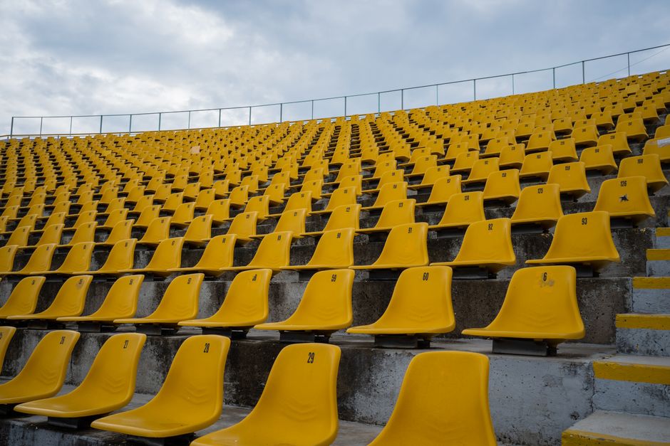 View of empty yellow seats arranged in rows at a stadium on a cloudy day.