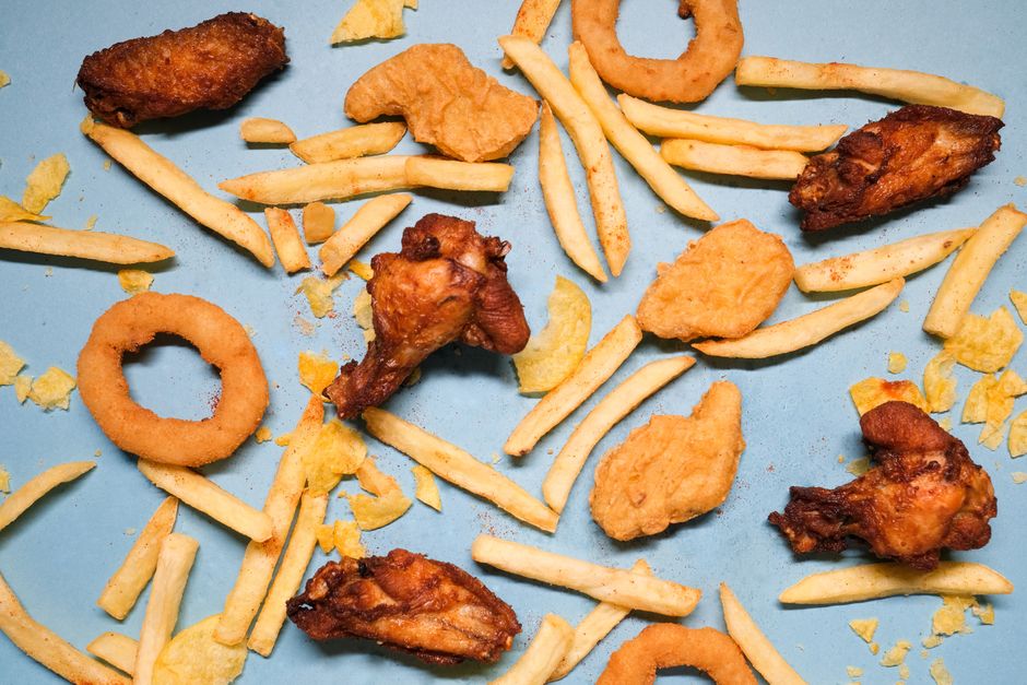 From above of french fries and grilled chicken wings with golden deep fried onion rings and nuggets with chips on blue background in bright studio