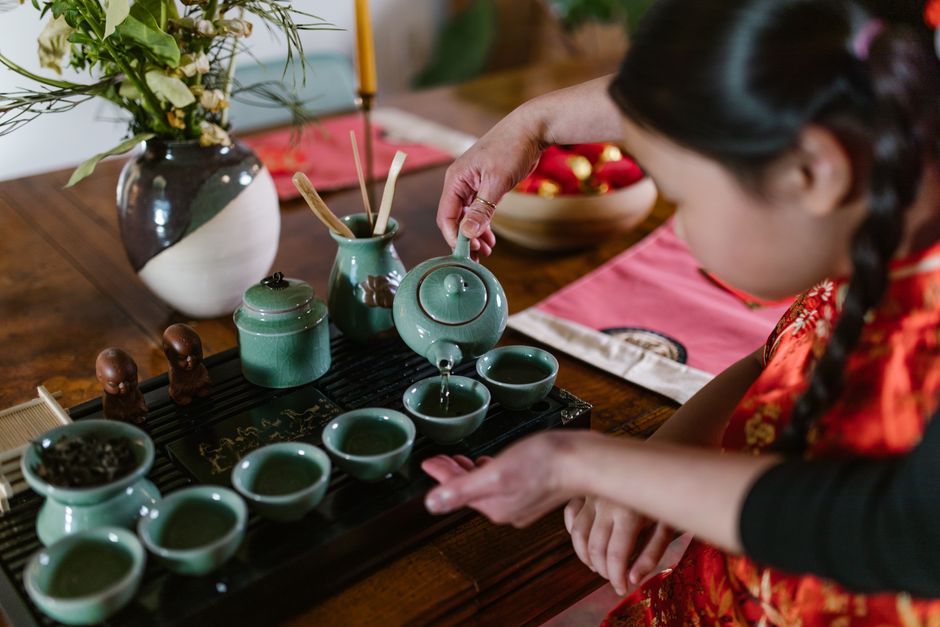 A young girl in traditional attire pours tea in a serene indoor setting.