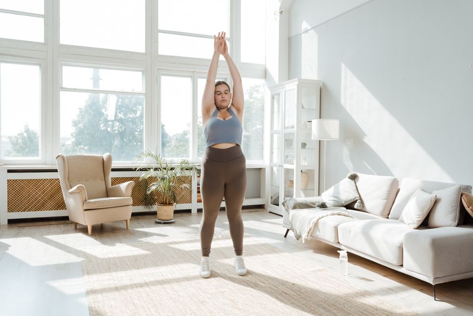 A woman practices stretching exercises in a sunlit living room, promoting wellness and healthy lifestyle.