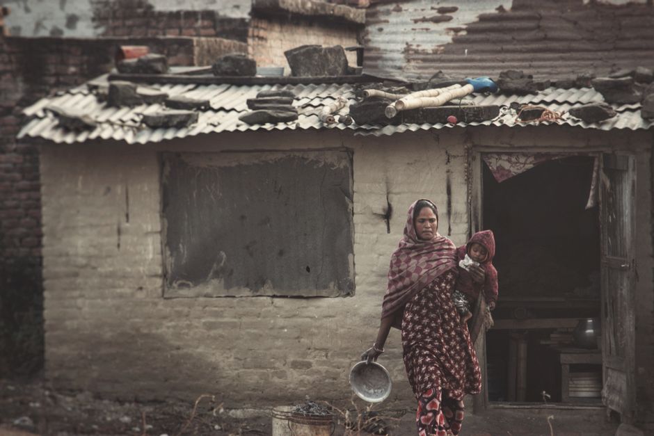 A traditional Nepali mother and child stand outside a rustic village house in Kathmandu.