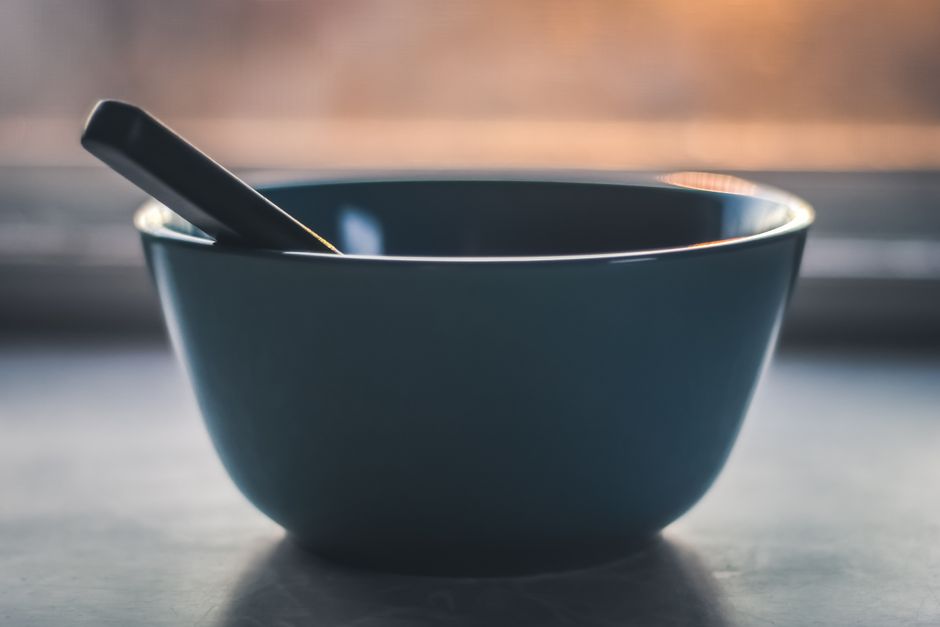 A minimalist photograph of an empty bowl with a spoon, set against a soft sunrise backdrop.