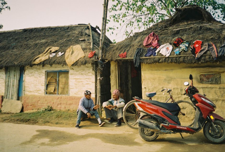 Two men having a conversation outside a traditional house with a motorcycle.