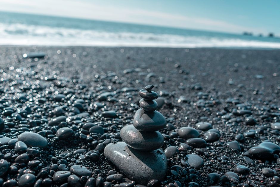 Tranquil scene of stacked stones on a black sand beach with the sea in the background.