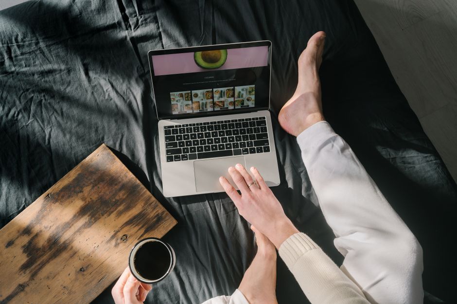 A relaxing scene showing a person using a laptop while holding coffee on a bed.