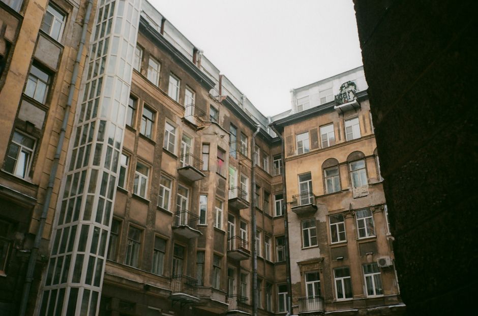 Low angle of weathered building exterior with windows and balconies under gray cloudless sky in daylight in town street