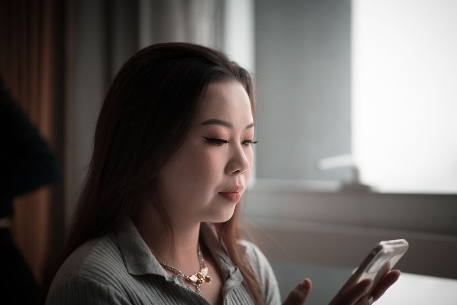Young Asian woman using smartphone indoors, focused on screen.