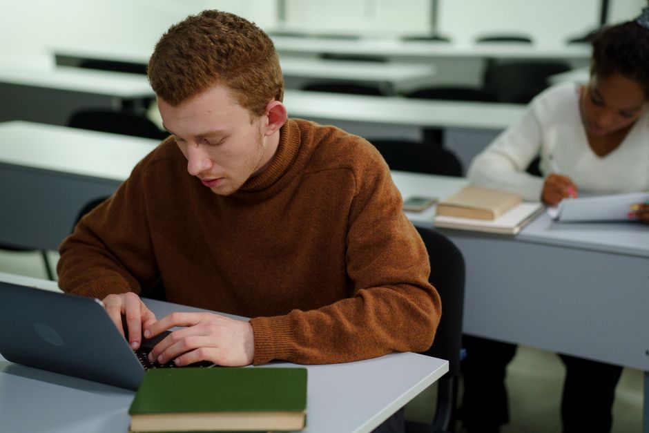Two students focusing on work in a classroom setting, using laptops.