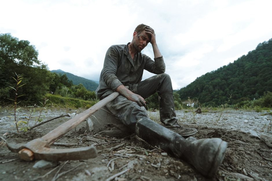 A tired male miner sits on rocky ground with a pickaxe, showcasing hard work and exhaustion.