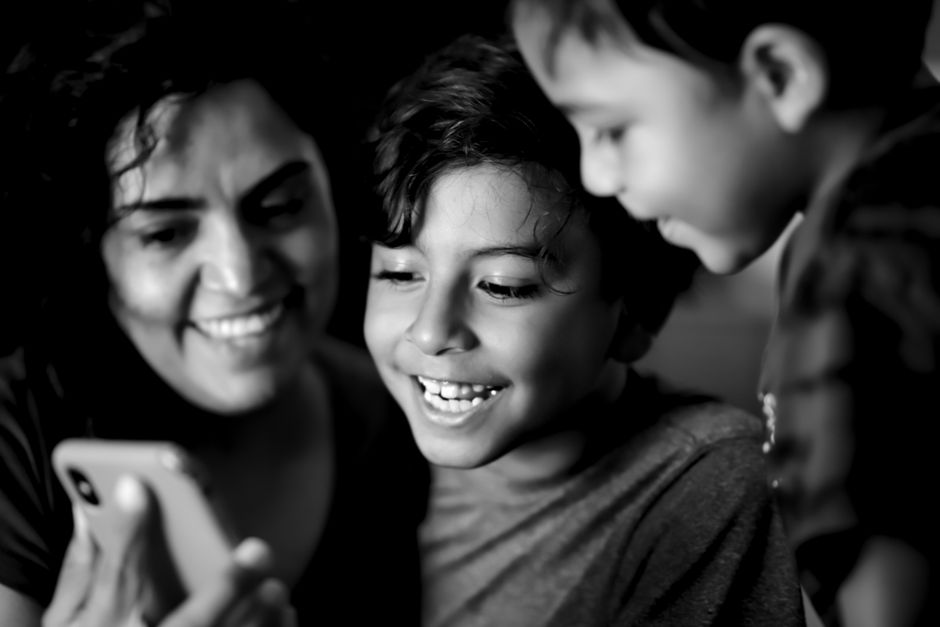 A joyful family moment with children and woman smiling at a phone screen, in black and white.