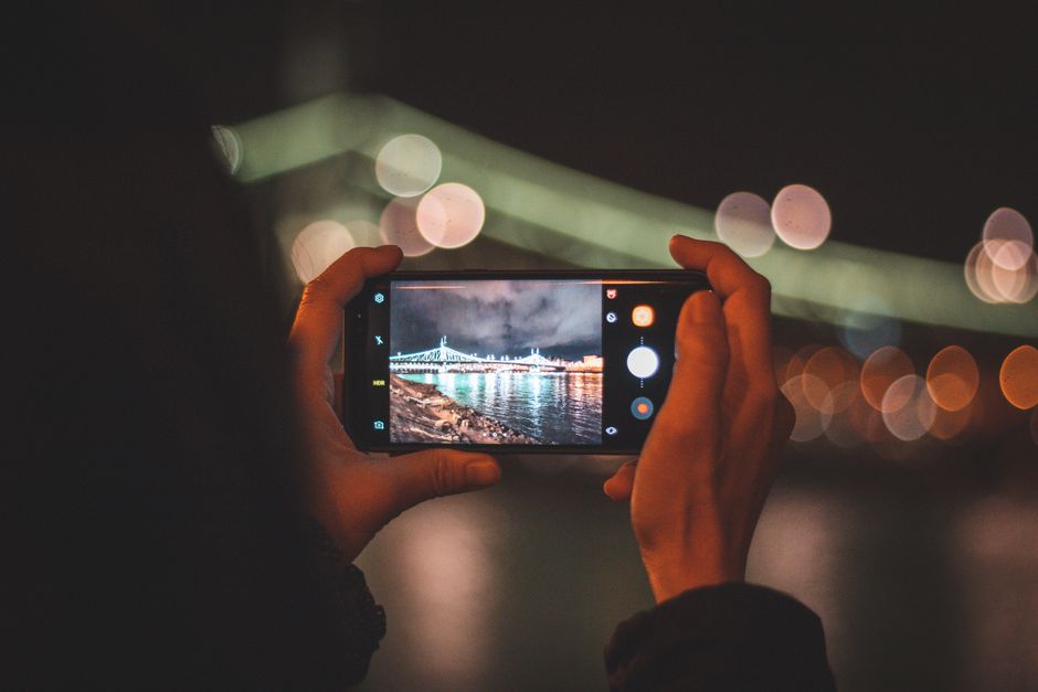 Hands holding a smartphone capturing a cityscape at night with colorful bokeh lights.