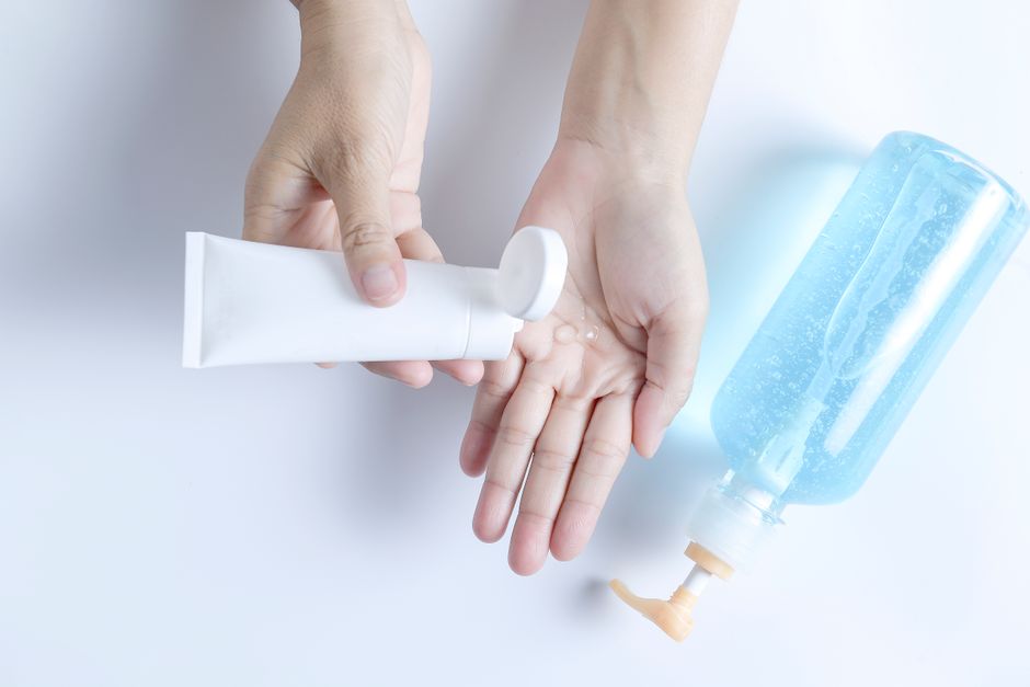 Hands using a white tube and blue bottle for skincare product application on a white background.