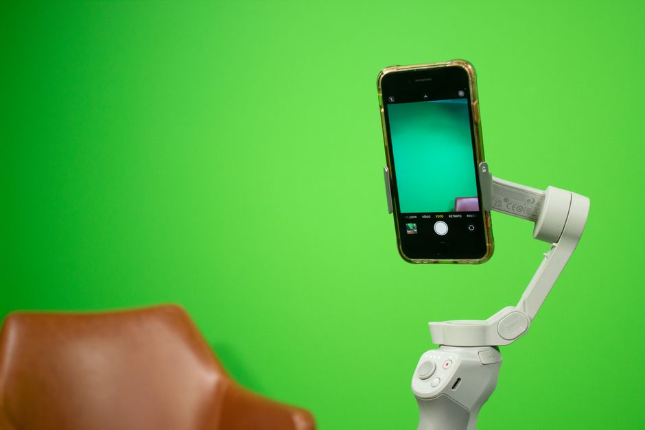 Smartphone mounted on a stabilizer in front of a green screen setup for video production.