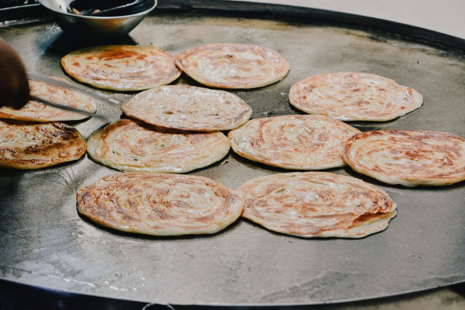 Close-up of golden parathas being cooked on a tawa, showcasing traditional South Asian street food.