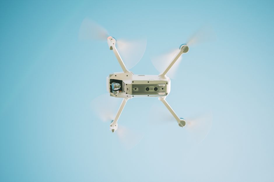 A sleek white drone flying under a clear blue sky, capturing aerial views.