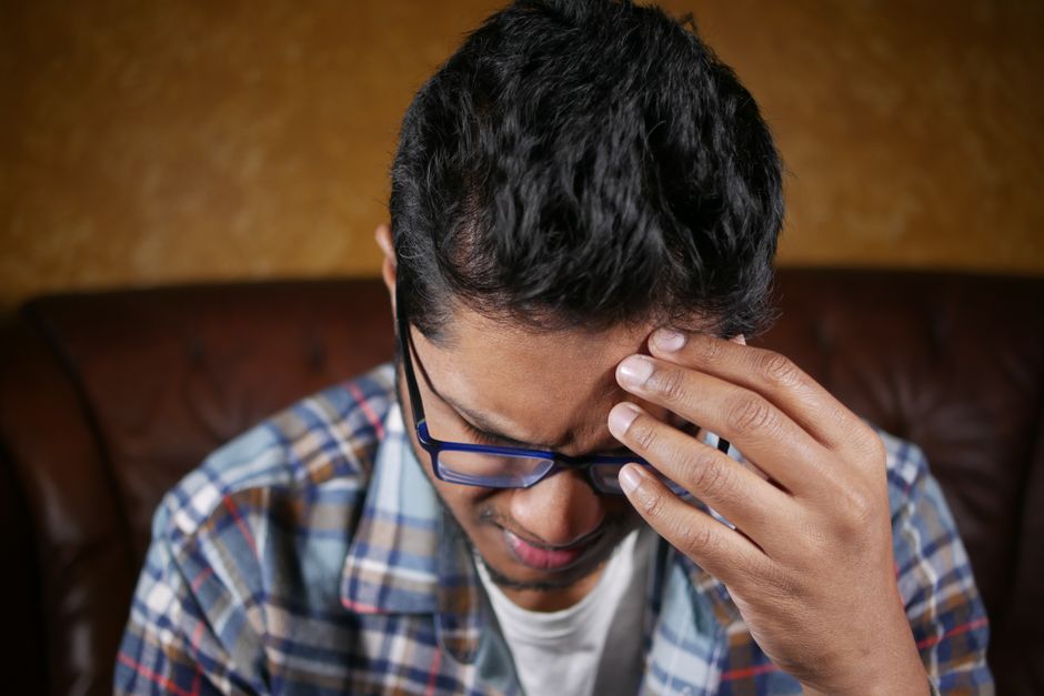 Close-up of a man wearing glasses, holding his head in pain, possibly experiencing a headache.