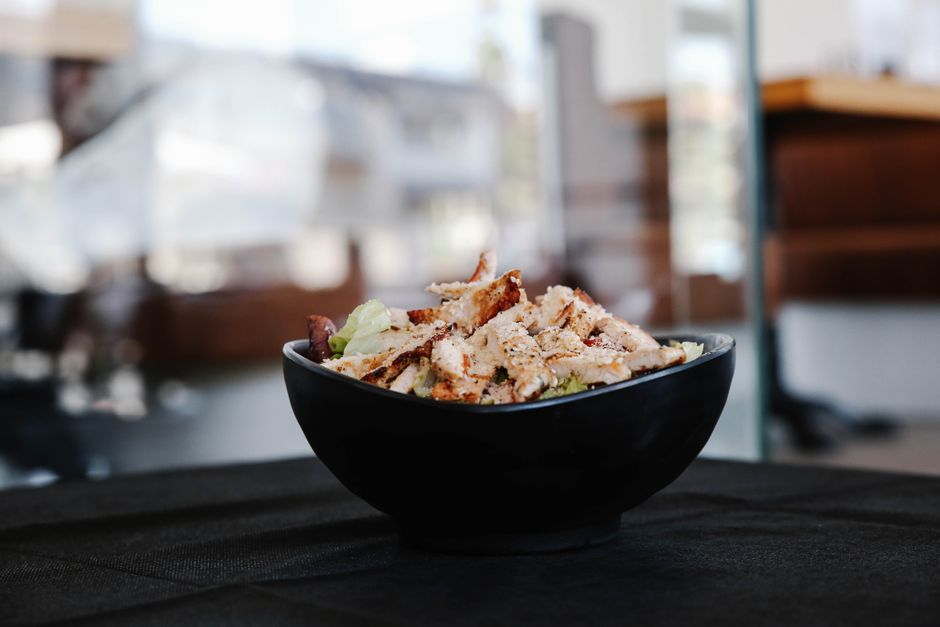 Savor this close-up of a grilled chicken salad in a stylish black bowl indoors.