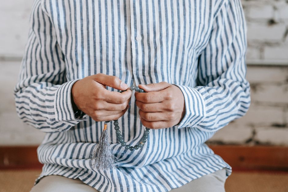A person wearing a striped shirt holds prayer beads close, symbolizing faith and meditation.