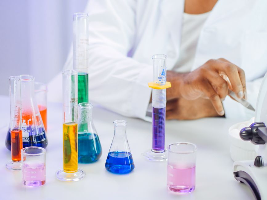 A scientist's hand working with colorful liquids in a laboratory setting.