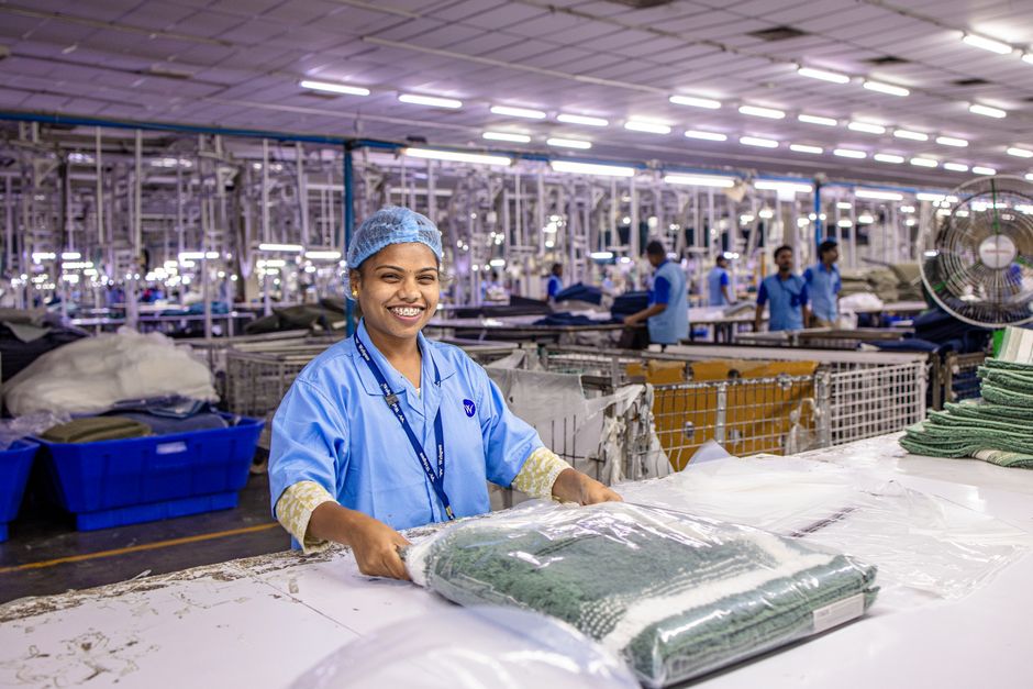 Smiling factory worker in modern textile plant packaging garments.