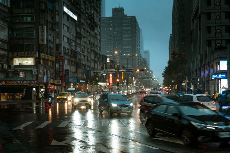 A bustling city street in the rain with cars and bright lights at dusk.