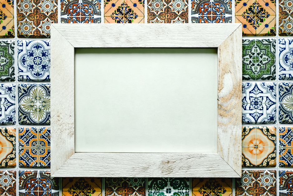 A blank wooden photo frame set against vibrant patterned mosaic tiles.