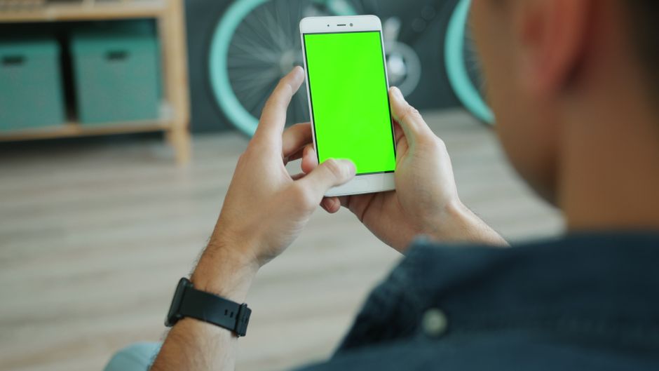 Close-up of hands holding smartphone with green screen indoors. Ideal for mockups.