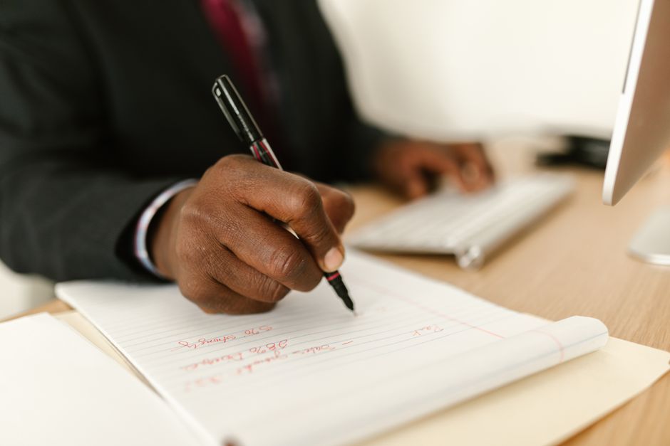 Close-up of a businessman writing notes in a notepad at a desk, highlighting stationary and productivity.
