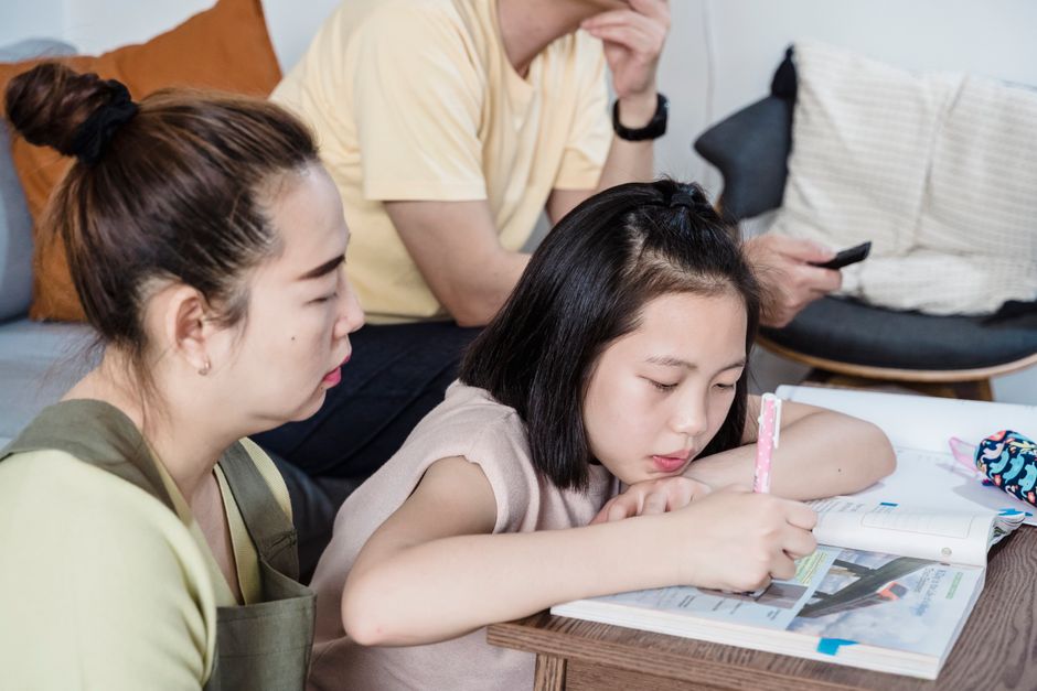 A mother guides her daughter through homework at home, fostering education and bonding.