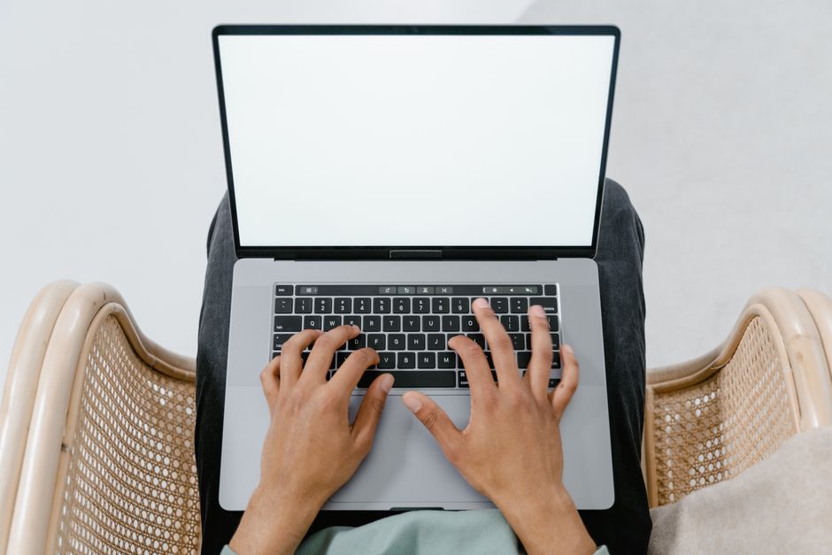 A person typing on a laptop with a blank screen, viewed from above in a casual setting.