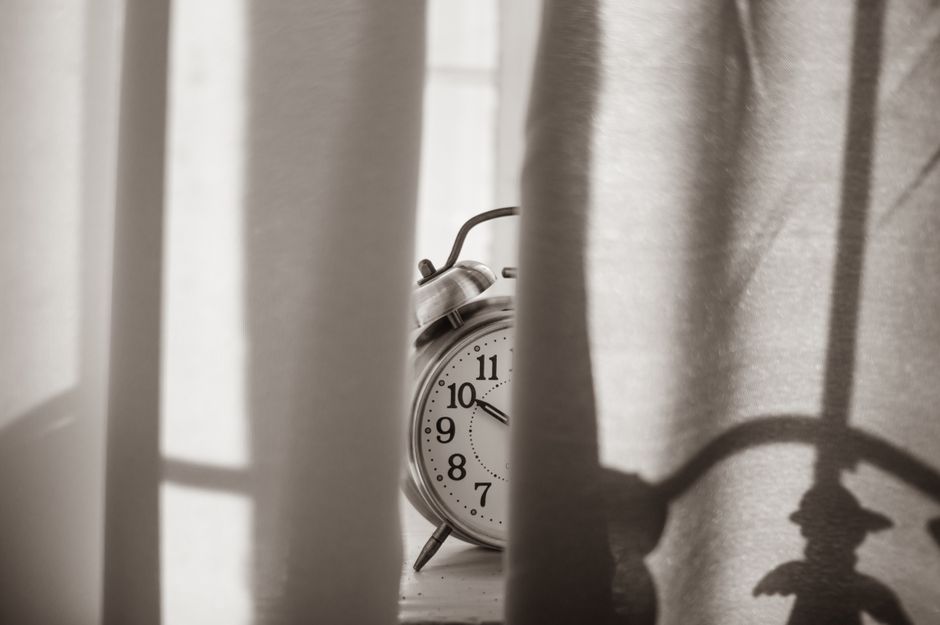 Monochromatic image of a vintage alarm clock peeking through curtains, conveying a sense of nostalgia.