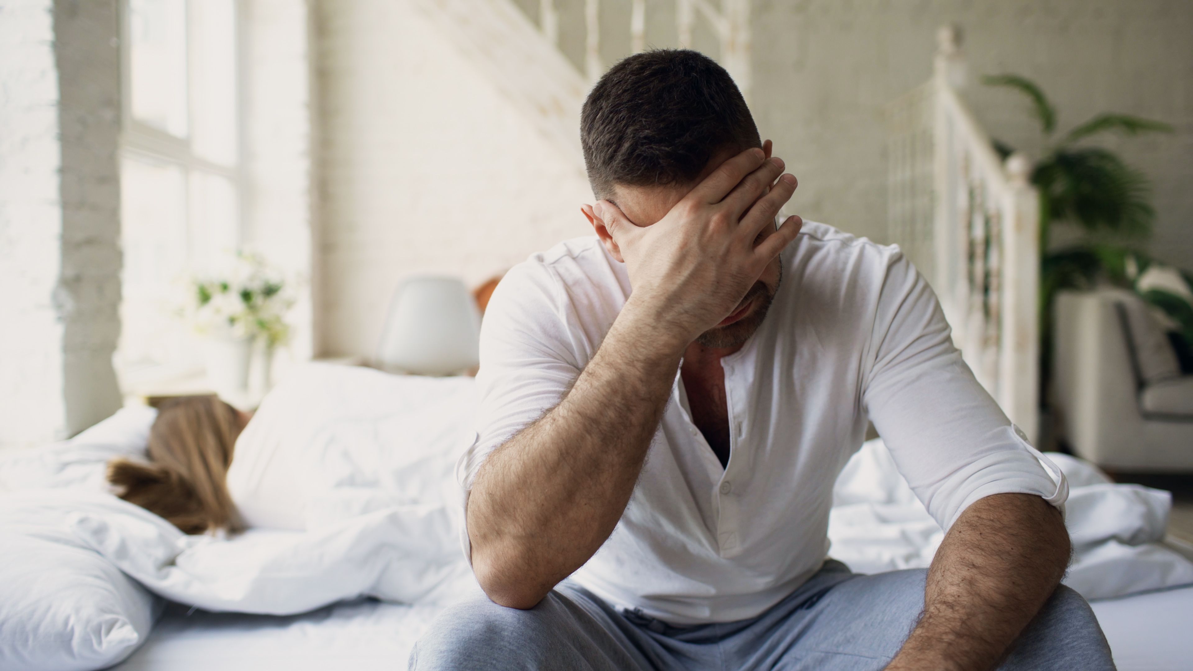 A tired person sitting on the bed in the morning, illustrating how poor sleep quality and other factors can cause fatigue even after eight hours of sleep.