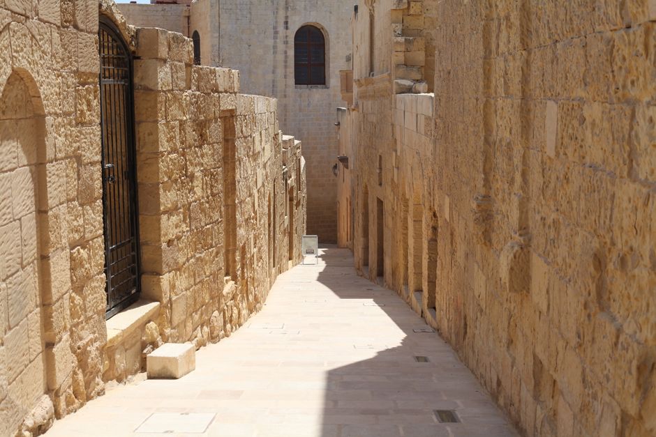Explore a sunlit ancient stone alleyway lined with historic buildings, exuding timeless architectural charm.