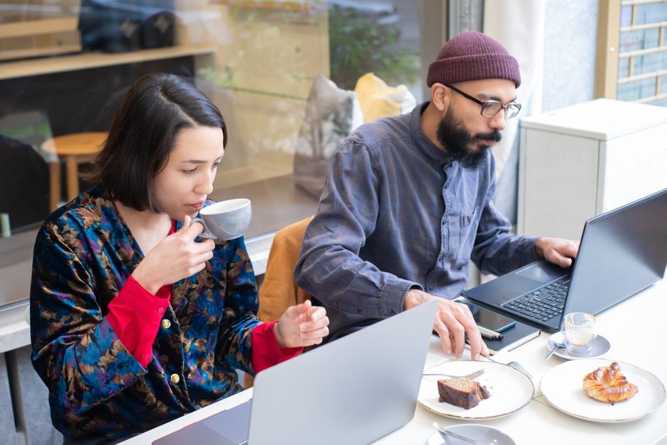 Two adults working on laptops in a contemporary café, enjoying coffee and pastries.
