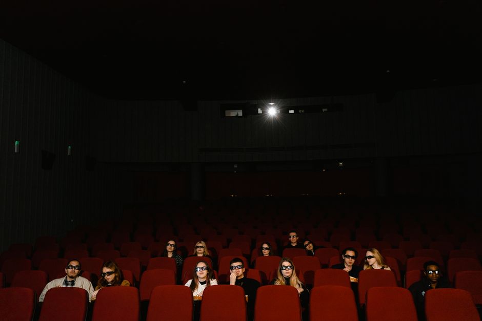 A group of people in a cinema watching a 3D movie wearing glasses, sitting in a dark theater.