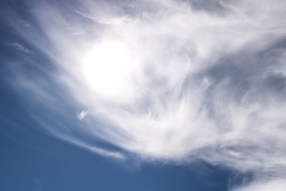 A serene view of the sun shining through delicate clouds against a vibrant blue sky.