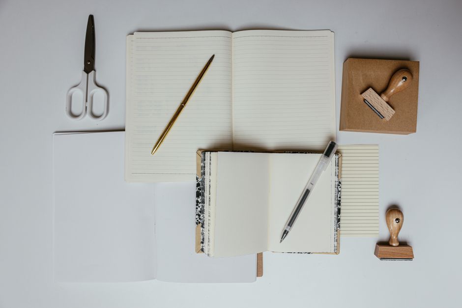 Flat lay of stationery including notebooks, pens, scissors, and stamps on a desk. Ideal for office or school themes.