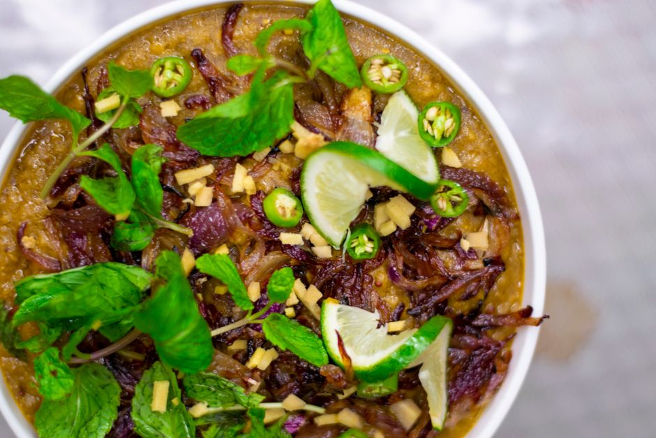 Close-up of a flavorful Haleem dish garnished with mint, lime, and chili peppers.
