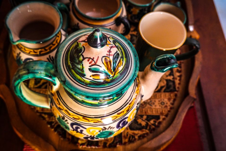 Vibrant handcrafted teapot and cups on an ornate wooden tray, showcasing detailed ceramic artistry.