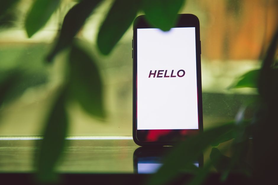 Smartphone with 'Hello' greeting on screen surrounded by green leaves, creating a fresh and tech-savvy ambiance.