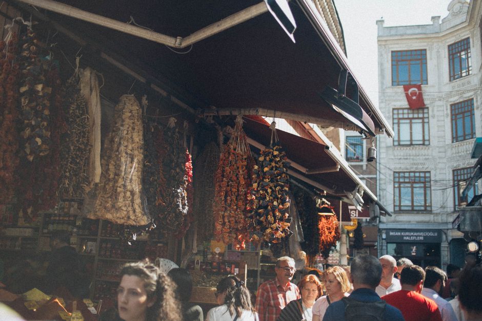 A vibrant market scene in Istanbul, showcasing hanging spices and a busy crowd under daylight.